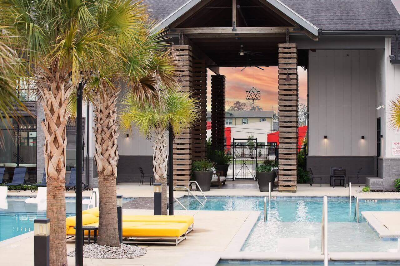 Wildwood Baton Rouge LSU Off-Campus Student Living Apartments: Resort-style Pool with Daybeds and Palm Trees with Clubhouse in Background 2