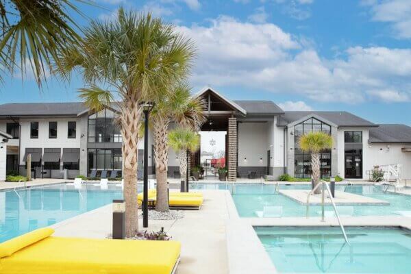 Wildwood Baton Rouge LSU Off-Campus Student Living Apartments: Resort-style Pool with Daybeds and Palm Trees with Clubhouse in Background